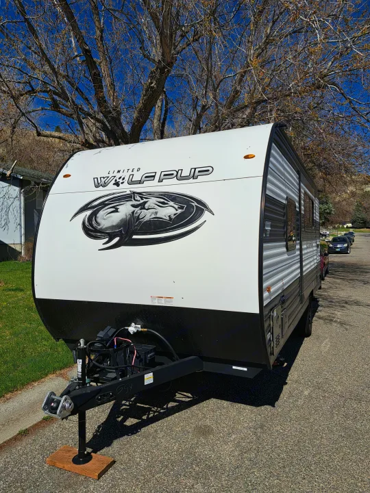 A white and black Limited Wolf Pup travel trailer with a wolf logo, parked on a sunny street, ready for rv rental.. Forest River Cherokee Wolf Pup 2023