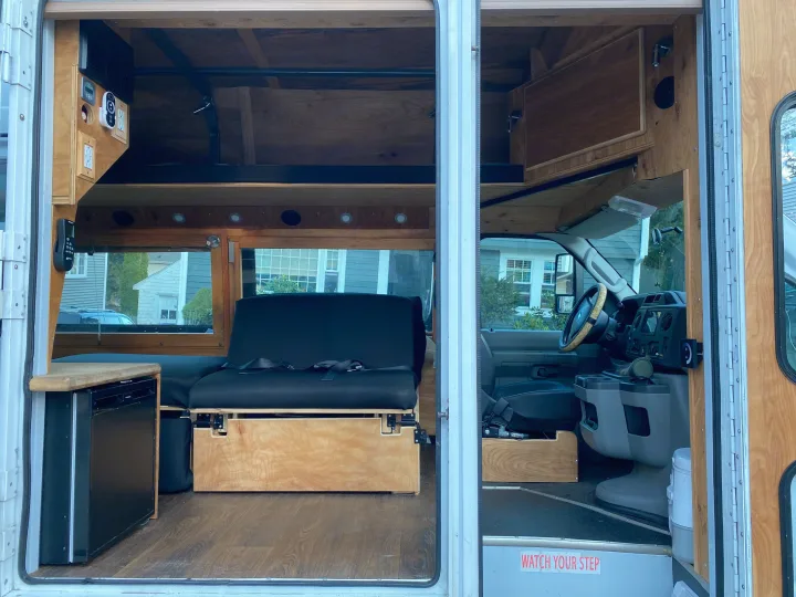 RV rental: Custom camper van interior with warm wood finishes, versatile seating/bed, mini-fridge, and driver's cab.. Ford Econoline 2011
