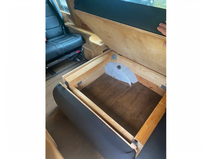 This RV rental offers clever storage: a lifted wooden platform reveals internal space beside plush seating and a vehicle seat.. Ford Econoline 2011