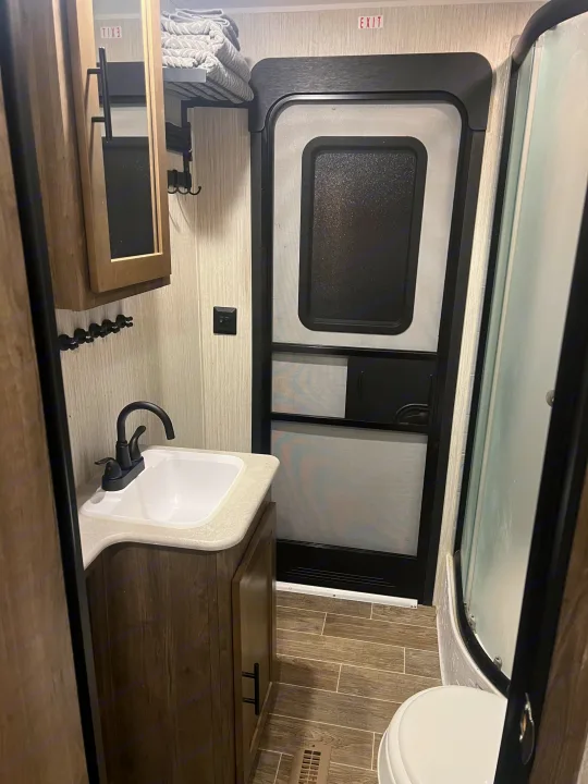 Compact RV rental bathroom with vanity, sink, toilet, and shower stall. An 'EXIT' sign is above the RV's main entry door.. Forest River Palomino Puma 2021