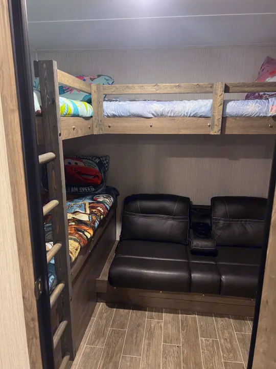 RV rental: Interior shows bunk beds with cozy bedding and a dark leather loveseat on wood-look floors.. Forest River Palomino Puma 2021