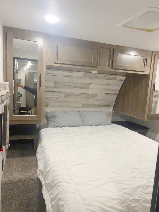 Compact RV rental bedroom with a comfy bed, overhead cabinets, and mirrored closet. Perfect for adventures.. Forest River Palomino Puma 2021