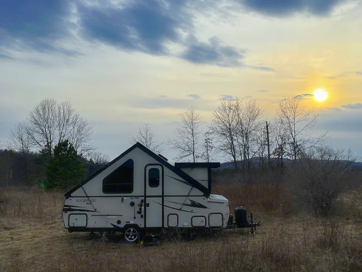 RV rental: An A-frame camper is parked in a vast, dry field at sunset, ready for quiet outdoor adventures.. Forest River Rockwood Premier 2019
