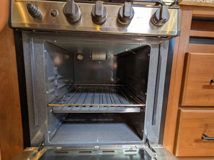 Open RV rental oven, clean interior with a single rack. Stove top and controls are above.. Outdoors RV Timber Ridge 2022