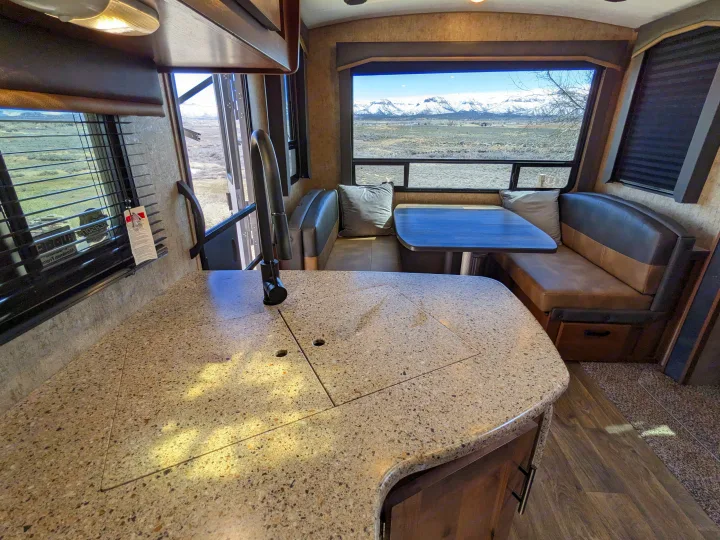 Spacious rv rental interior featuring a kitchen counter, dining booth, and stunning mountain views from large windows.. Outdoors RV Timber Ridge 2022