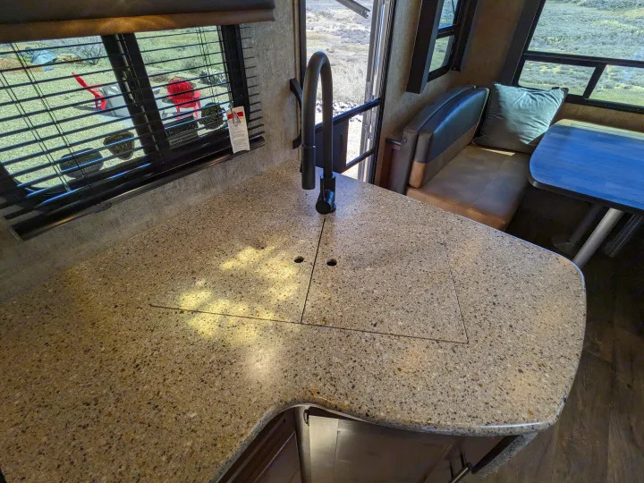 Bright RV rental kitchen with speckled countertop, integrated sink, and dinette. Window offers an outdoor view.. Outdoors RV Timber Ridge 2022
