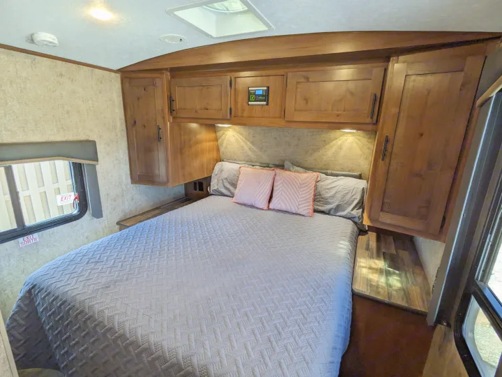 Cozy RV rental bedroom featuring a comfy bed, overhead cabinets, and emergency exit window for your next adventure.. Outdoors RV Timber Ridge 2022