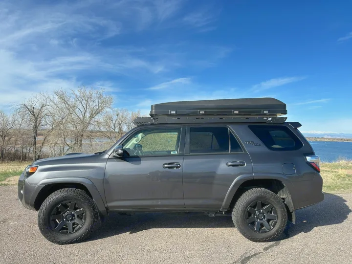 Side view of a dark gray Toyota 4Runner SUV with a rooftop tent by a lake. Perfect for adventure, a unique RV rental alternative.. Toyota 4Runner TRD OffRoad 2020