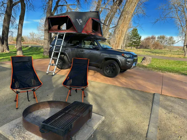 Fully equipped campsite with a gray SUV, rooftop tent, and ladder. Two chairs & fire pit are ready. Great for RV rental style adventures.. Toyota 4Runner TRD OffRoad 2020