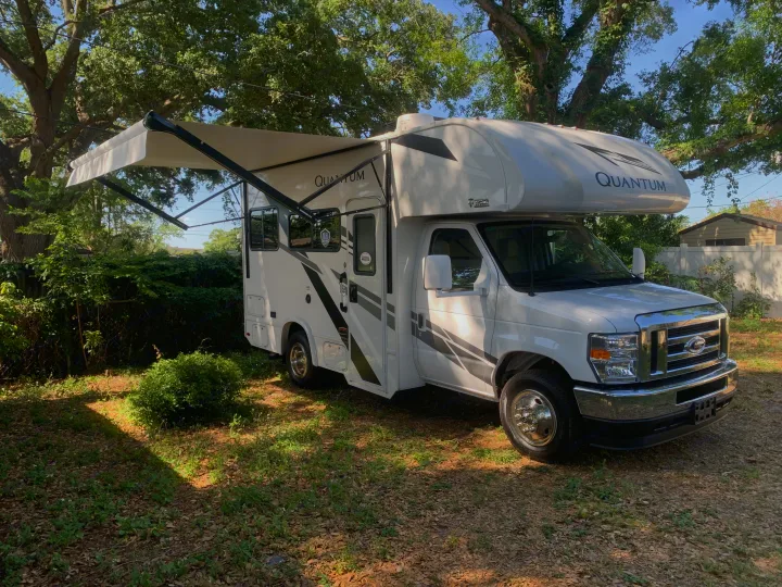 White Quantum Class C rv rental with awning extended, parked in a sunny, grassy outdoor setting.. THOR THOR QUANTUM LC19 2025