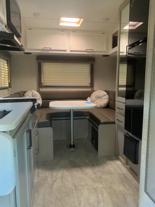 Bright and modern RV rental interior showcasing a U-shaped dinette, compact kitchen, and overhead storage.. THOR THOR QUANTUM LC19 2025