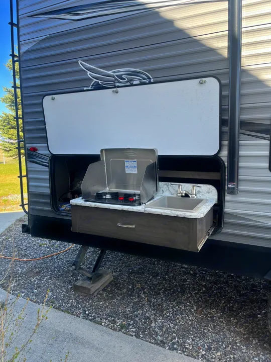 An RV rental's side view reveals a pull-out outdoor kitchen with a stove and sink, ideal for camping adventures.. Jayco Jay Flight SLX Rocky Mountain Edition 2021