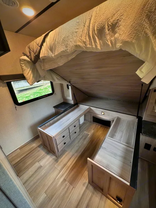 RV rental: Bed lifted to reveal under-bed storage, wooden cabinets, and light wood-look flooring in a compact interior.. Forest River Coachmen Northern Spirit Ultra Lite 2023