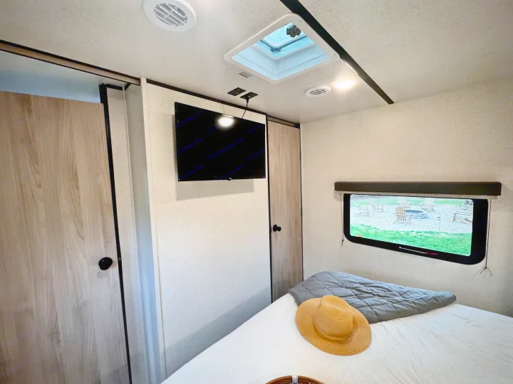 Inviting RV rental bedroom with a bed, TV, and doors. Enjoy the skylight and fire pit view outside.. Forest River Coachmen Northern Spirit Ultra Lite 2023