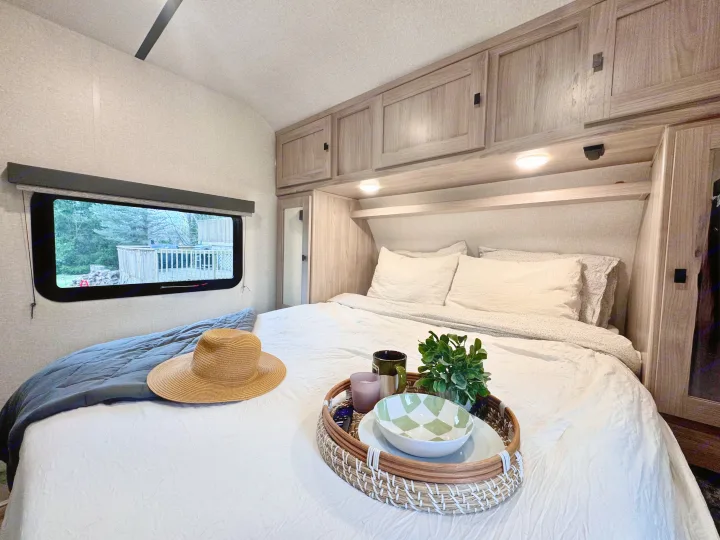 Inviting RV rental bedroom with a neatly made bed, decorative tray, overhead storage, and window showcasing the outdoors.. Forest River Coachmen Northern Spirit Ultra Lite 2023