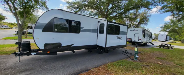 A white & black Wildwood Platinum travel trailer RV rental, parked with power hooked up at a sunny campground site.. Forest River Wildwood Platinum 2024