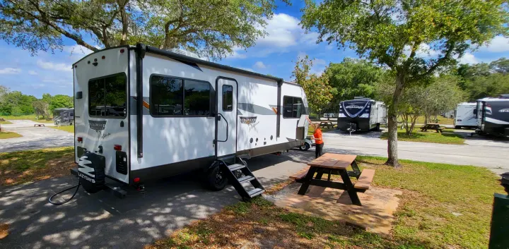A white rv rental travel trailer is parked at a sunny campsite with a picnic table, ready for outdoor adventures.. Forest River Wildwood Platinum 2024