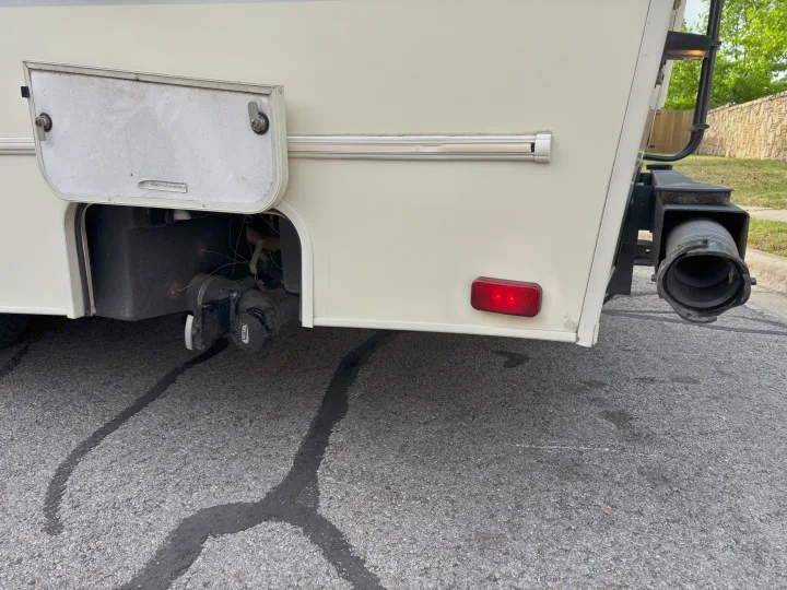 RV rental's rear: open compartment shows wastewater tanks and plumbing, with dark liquid leaking onto the pavement.. Forest River Coachmen Freelander Micro 2018