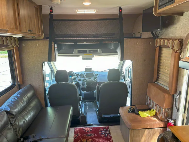 Experience this clean RV rental interior: forward view into the driver's cabin, complete with sofa, dinette seating, and a mesh bunk safety net.. Forest River Coachmen Freelander Micro 2018