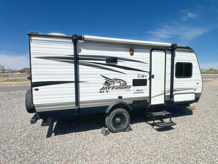 White and black Jay Flight SLX Baja Edition travel trailer for rv rental, parked on gravel under a clear sky.. Jayco Jay Flight SLX Baja Edition 2017