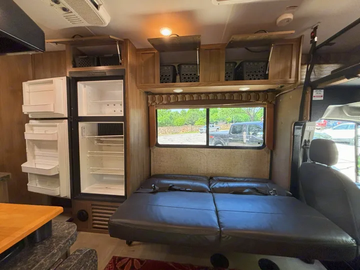Clean RV rental interior: large empty fridge, modular sofa/bed with seatbelts, open overhead cabinets with storage.. Forest River Coachmen Freelander Micro 2018