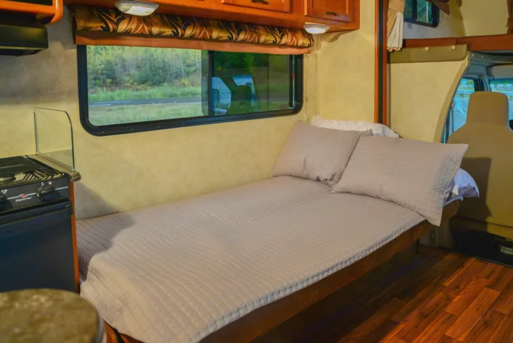 Compact RV rental interior featuring a cozy bed, small kitchen, and window view for comfortable travel.. Forest River Coachmen Freelander 2014