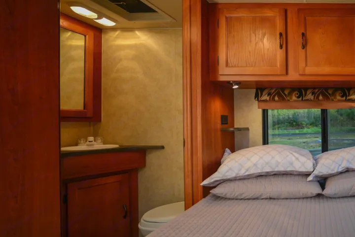 RV rental interior: bedroom with bed & cabinets, alongside a bathroom with sink & toilet.. Forest River Coachmen Freelander 2014