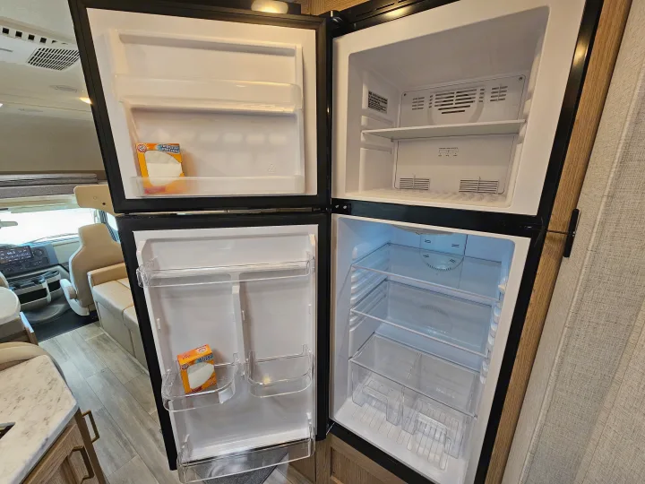 An open, empty refrigerator/freezer in an RV rental, with baking soda boxes on shelves, ready for your road trip provisions.. Thor Motor Coach Four Winds 2026