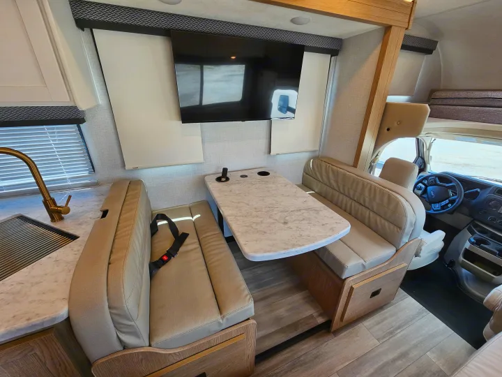 View of a modern **rv rental** interior showing a dinette, kitchen, TV, and driver's cab. Perfect for trips!. Thor Motor Coach Four Winds 2026