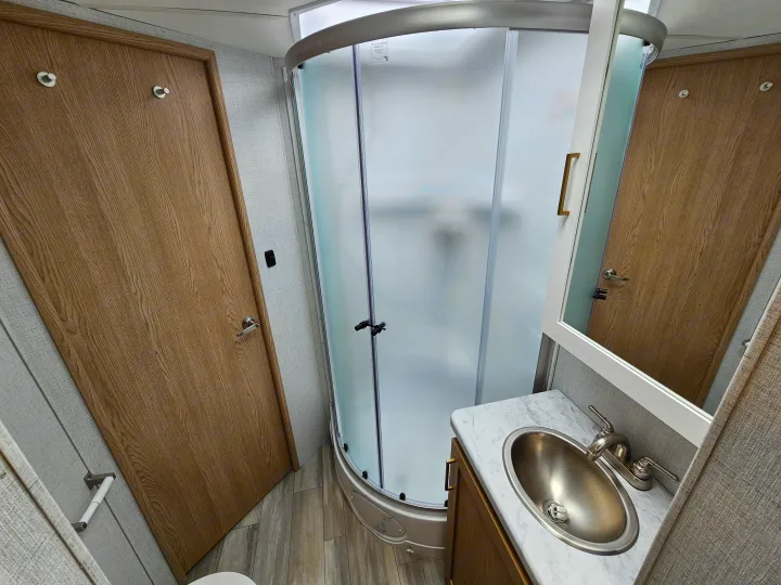 This RV rental features a compact bathroom with a frosted glass corner shower, sink, and toilet, maximizing space.. Thor Motor Coach Four Winds 2026