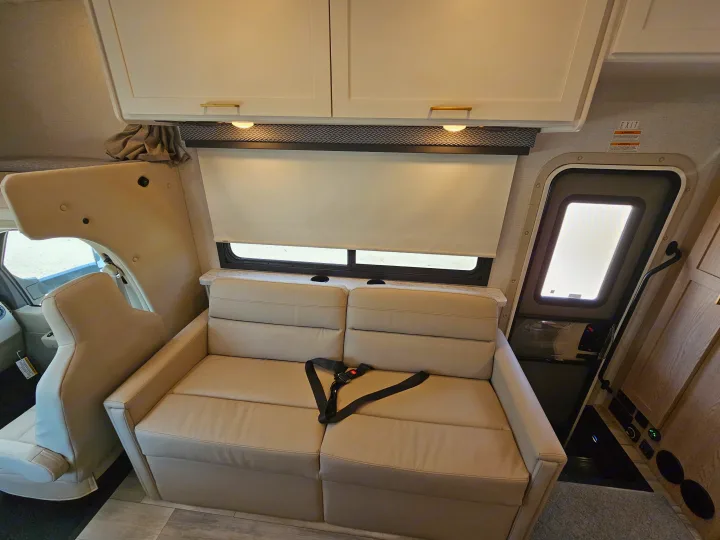 RV rental: Comfortable interior living area with light-colored sofa, cabinets, window, and exit door.. Thor Motor Coach Four Winds 2026