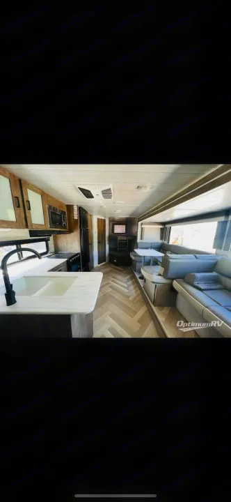 View inside an RV rental: modern kitchen on left, central passage, large living area with L-shaped sofa and dinette on right.. Forest River Wildwood X-Lite 2022