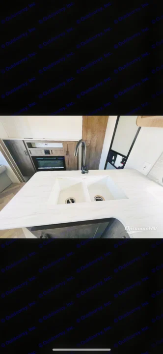 RV rental kitchen: modern white countertop, double sink, and built-in oven, ideal for your next trip.. Forest River Wildwood X-Lite 2022