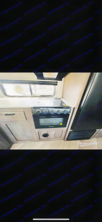 RV rental kitchen: light wood cabinetry, white countertop, window, Greystone stove/oven, and refrigerator.. Forest River Wildwood X-Lite 2022
