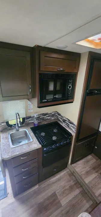 RV rental kitchenette: stainless steel sink, gas stove, built-in microwave, dark cabinets & tiled backsplash.. Thor Motor Coach Ford E350 2018