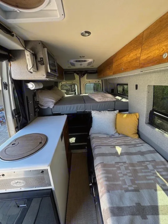 Inside an RV rental: a cozy camper van interior with a galley, elevated rear bed, and side bench/bed.. Storyteller Overland Beast 2023