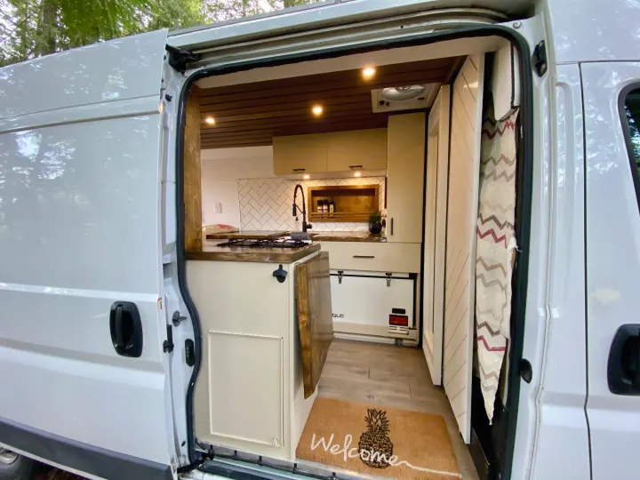Inside this modern RV rental van, a bright kitchen features subway tile, stove, sink, and a cozy welcome mat.. Ram Promaster 2018