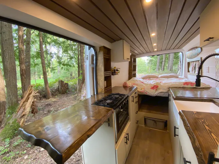 Cozy RV rental camper van with a full kitchen, comfortable bed, and scenic forest views outside.. Ram Promaster 2018