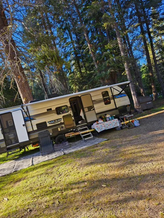 Ideal RV rental setup at a woodsy campsite! Features a spacious travel trailer with awning, outdoor seating, and a grill area.. Forest River Salem 2021