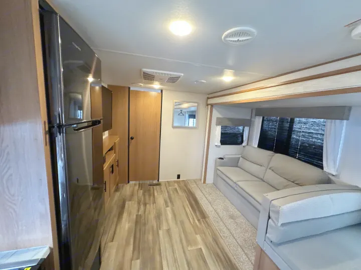 Spacious RV rental interior: modern fridge, light wood cabinetry, a gray sofa by windows, and wood-look flooring.. Fmc Primetime 2022