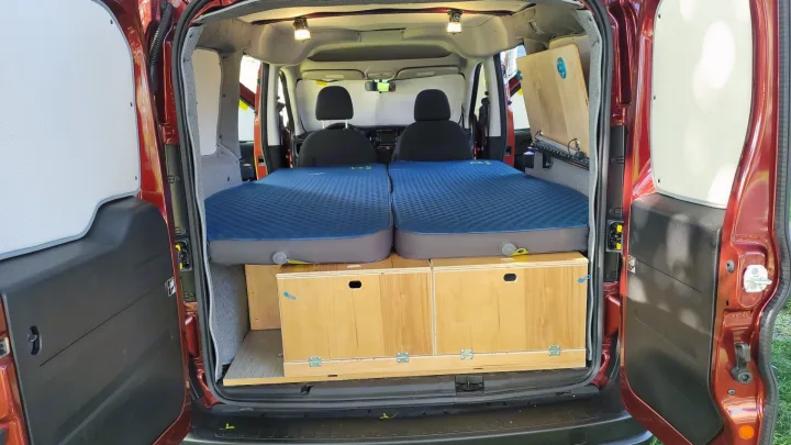 Explore a compact rv rental camper van: rear view showing two inflatable beds above wooden storage units, ready for camping.. RAM Promaster CIty 2018