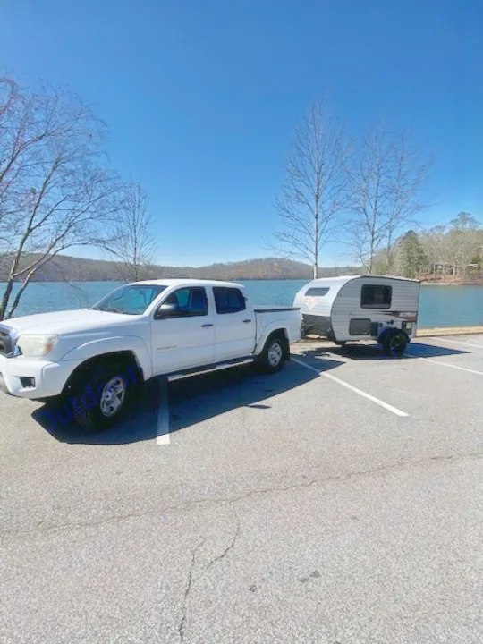 Scenic lake view with a white pickup towing an RV rental. Perfect for outdoor adventures!. Sunset Park RV SunRay 2019