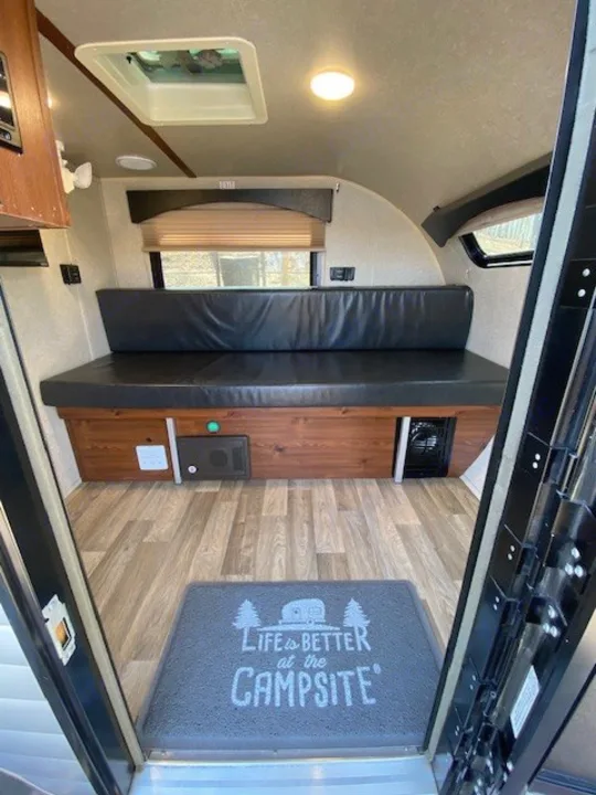 Step inside this inviting RV rental interior: a comfy bench bed, wood-look flooring, and a fun "Campsite" mat welcome you.. Sunset Park RV SunRay 2019