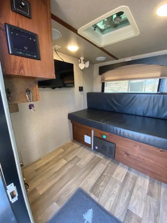 RV rental interior: cozy living space with wood flooring, a black dinette, TV, and control panel. Perfect for travel!. Sunset Park RV SunRay 2019