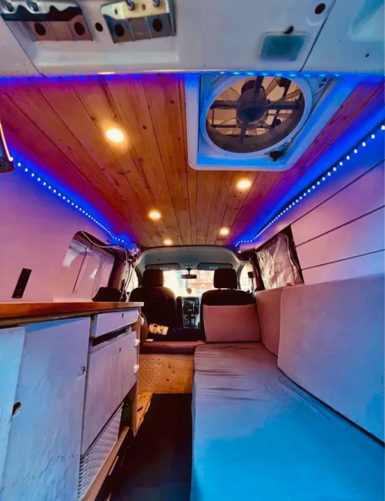 Explore this cozy RV rental! Custom camper van interior with wood ceiling, fan, blue LEDs, kitchen unit, and comfortable bed.. Nissan NV200 2015