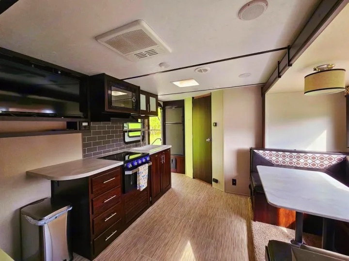 Bright RV rental interior: A modern kitchen with TV, stove, microwave, sink, and comfortable dinette area.. Forest River Tracer Breeze 2020