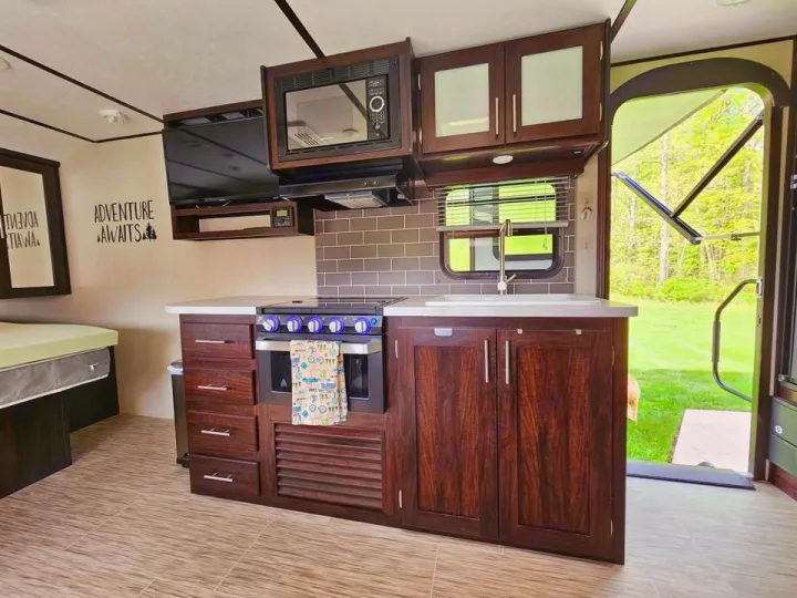 This RV rental's spacious interior highlights a well-equipped kitchen with stove, microwave, and sink, plus a TV and bed, all leading to nature.. Forest River Tracer Breeze 2020