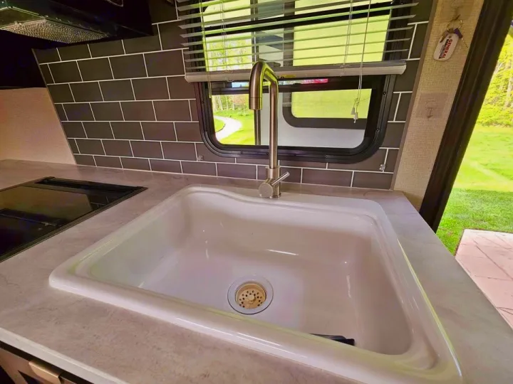RV rental interior: well-equipped kitchen with a white sink, compact cooktop, and dark subway tile backsplash.. Forest River Tracer Breeze 2020