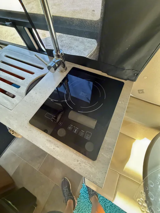 Compact RV rental kitchen features a modern induction cooktop, sink, and stylish countertop, ideal for travel.. Pleasure-Way Ascent 2021