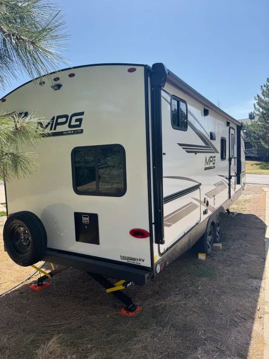 White MPG Ultra-Lite RV rental parked outdoors, showing the rear with spare tire and extended jacks.. Cruiser RV MPG 2500BH 2024